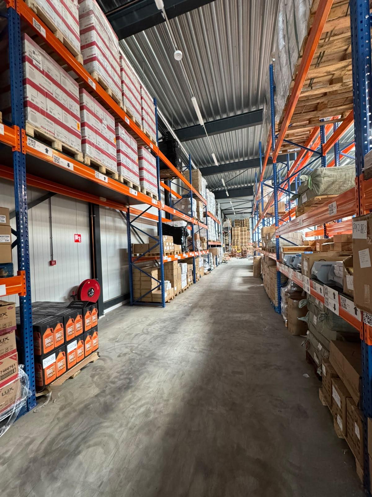 An aisle in the MIQ warehouse in Schiedam, with orange and blue pallet racking stocked with boxes and bales